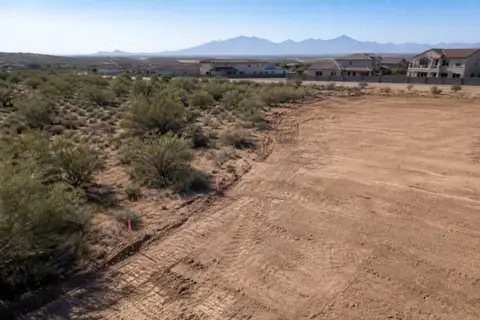 Half-cleared one-acre homesite with smooth pale dirt on one side, remaining mesquite scrub on the other, and survey stakes with pink flagging